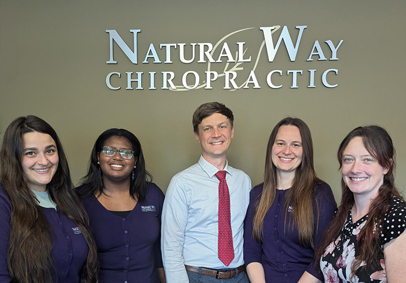 Oak-Harbor-Group Five staff members stand in front of a Natural Way Chiropractic sign, smiling at the camera.
