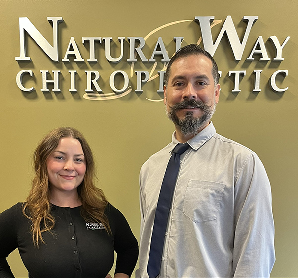 arlington-group-pic Smiling woman and man in business attire standing side by side in front of a wall sign that reads Natural Way Chiropractic.