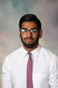 Formal portrait of a man with dark hair, a beard, and glasses wearing a white shirt and red patterned tie, facing the camera.