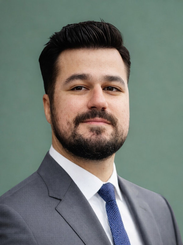Professional head-and-shoulders portrait: man in a gray suit and blue tie, slight smile, against a green background